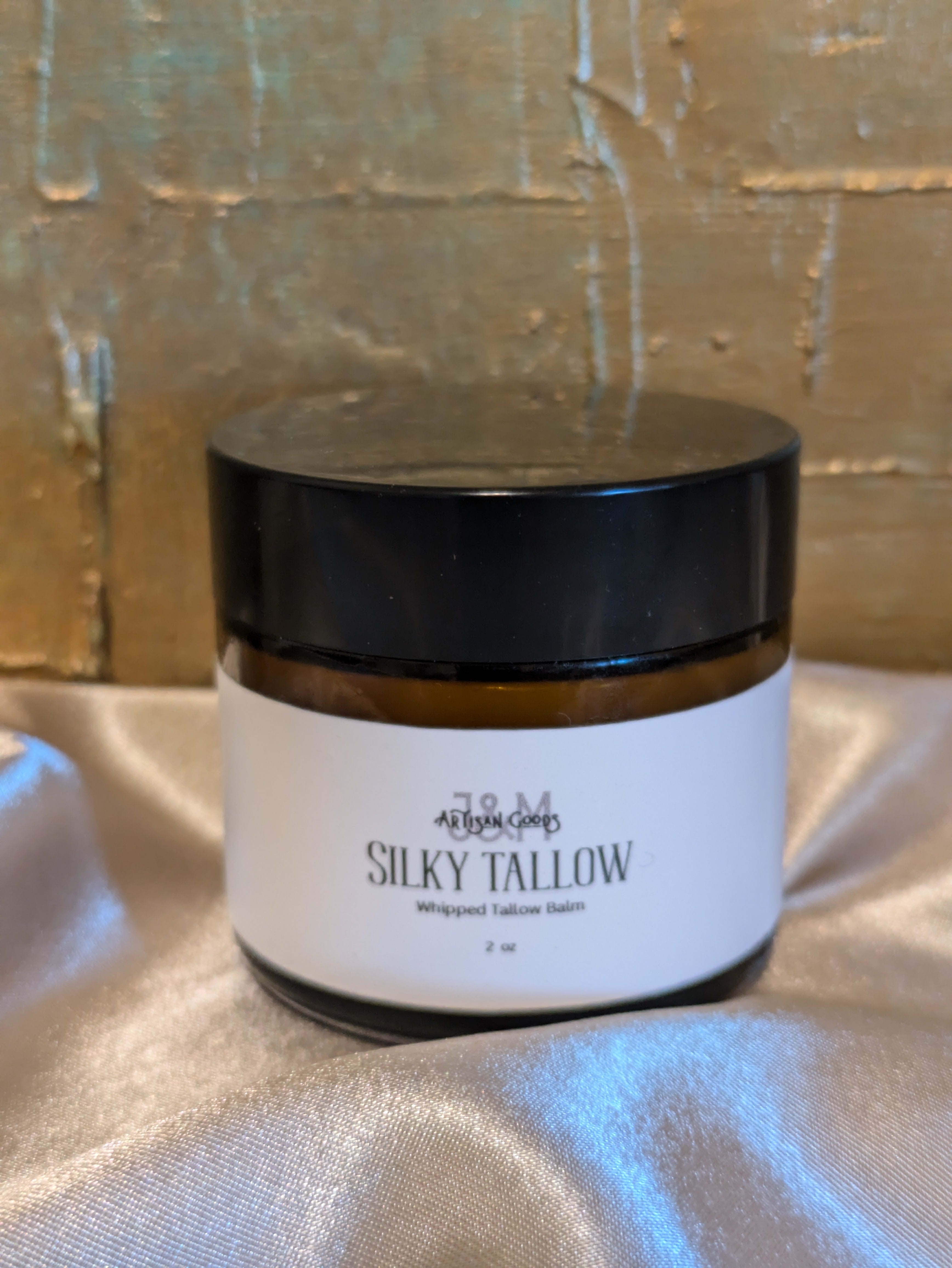 Jar of 'Silky Tallow' on a textured surface with a metallic background